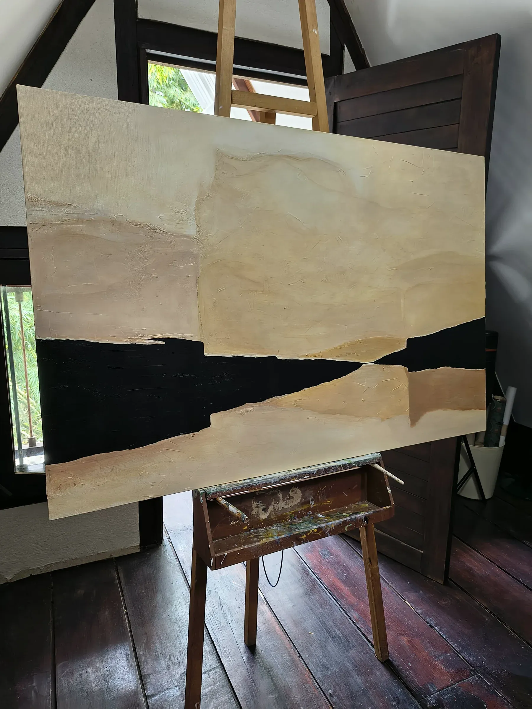 Pintura abstracta de capas beige y una franja negra, en el caballete del taller