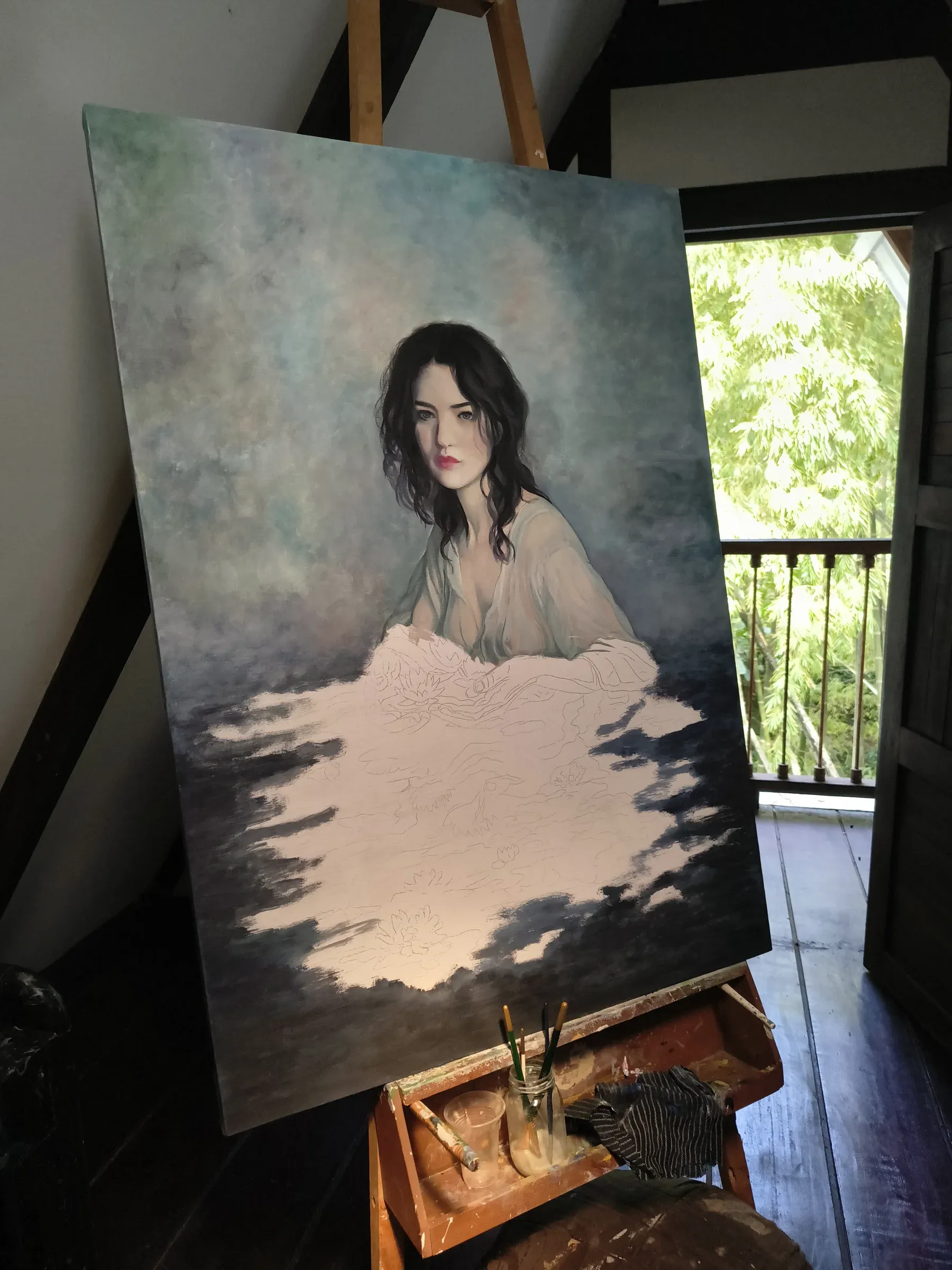 Retrato a medio pintar de una mujer de cabello oscuro sobre fondo azul brumoso, en el caballete junto al balcón